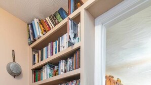 Un couloir avec une grande bibliothèque remplie de livres, un coin cuisine avec des meubles en bois et une table à manger avec des chaises.
