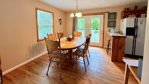 Un coin repas avec une table et des chaises en bois, un lustre, et une cuisine équipée d’un réfrigérateur et de placards.