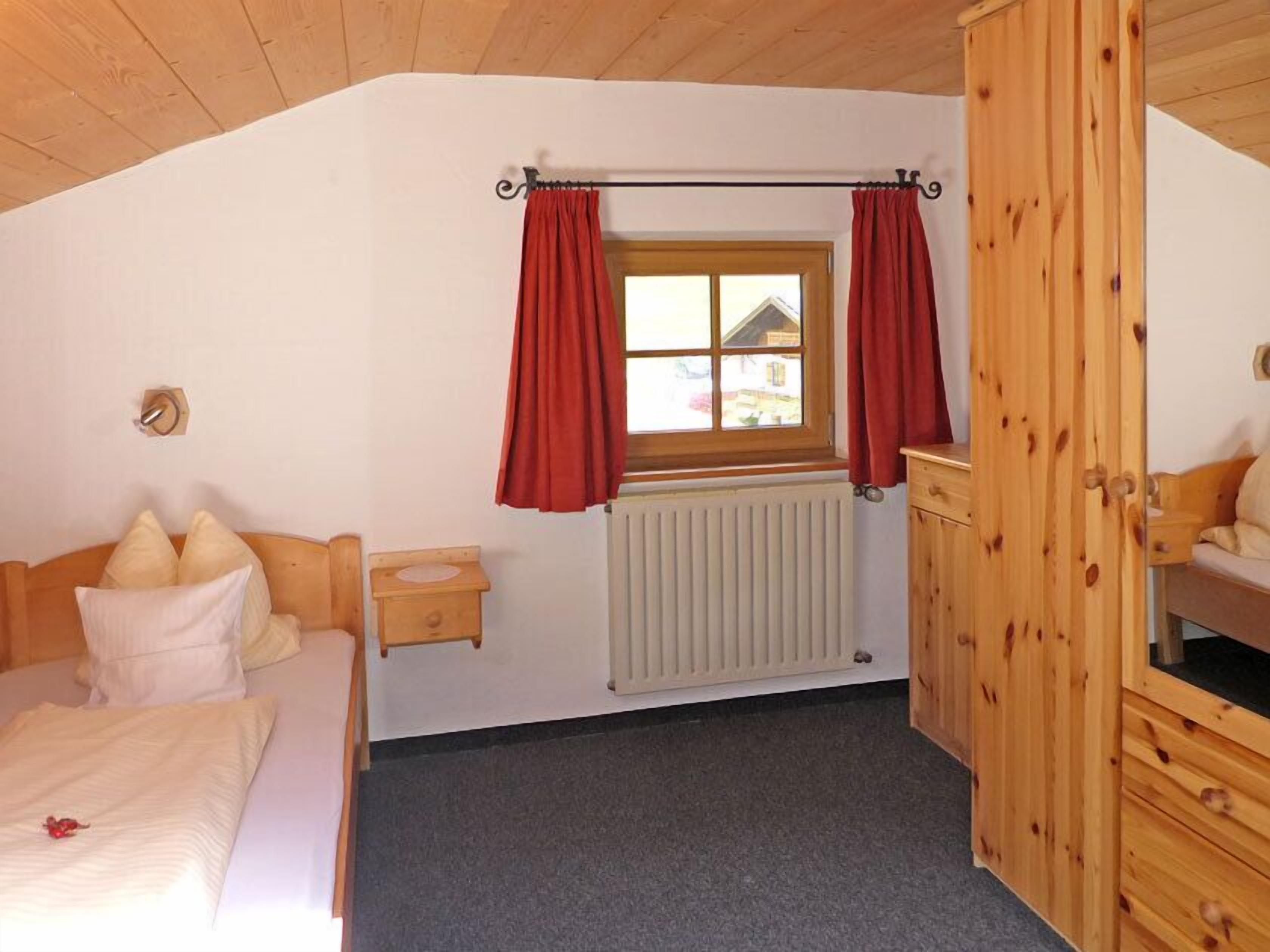 Une chambre à coucher avec un lit, une armoire en bois, une fenêtre avec des rideaux et un radiateur.
