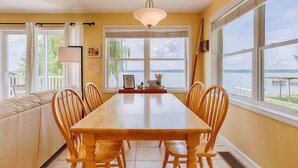 Un espace repas avec une table et des chaises en bois, de grandes fenêtres donnant sur un lac et un luminaire au plafond.