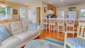Un salon chaleureux avec un canapé beige, une table basse et un tapis à motifs. On y trouve également un coin cuisine avec des meubles en bois, un réfrigérateur et une table à manger avec des chaises.