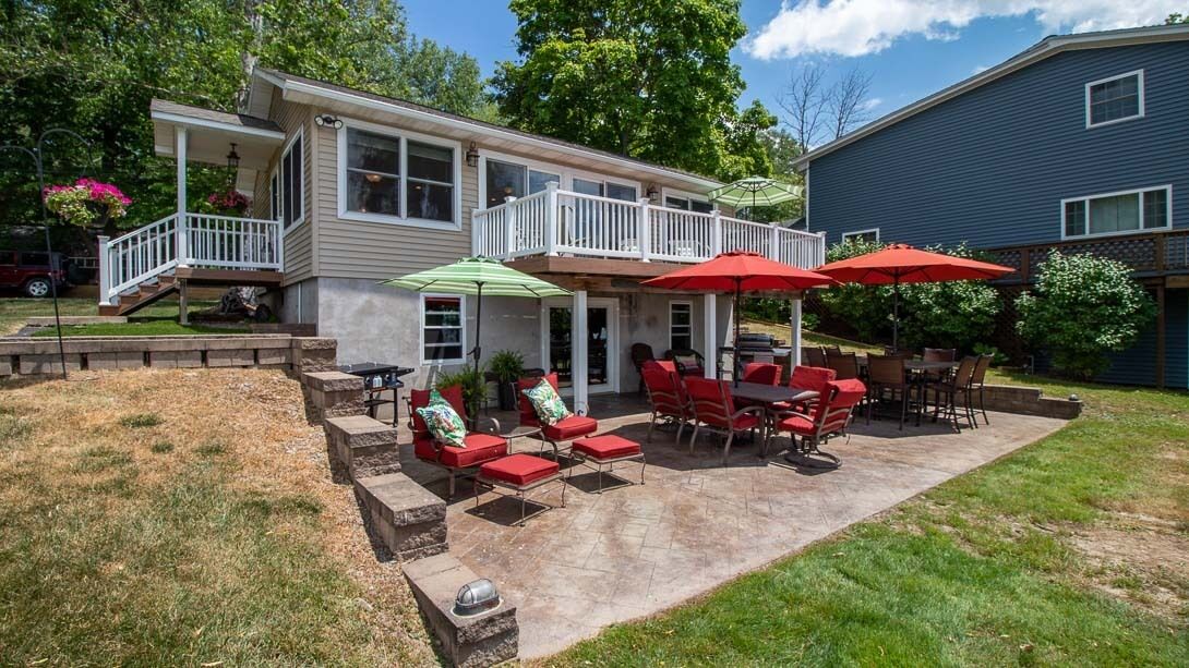 Une maison à deux étages dotée d’un patio couvert, agrémenté de parasols rouges et verts, de mobilier d’extérieur et d’un chemin en pierre.