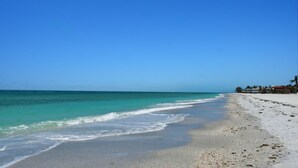 A beach with clear blue water, a sandy shore, and buildings in the background. - Steps to Beach-Full gulf views infinity pool-EXQUISITE! Ask @ seasonal specials! (Longboat Key)