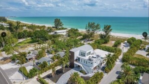An aerial view of a coastal property with a modern house, a beach, and surrounding greenery. - Steps to Beach-Full gulf views infinity pool-EXQUISITE! Ask @ seasonal specials! (Longboat Key)