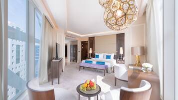 A modern hotel room with a large bed, a sitting area with a round table, and a view of the city through large windows.