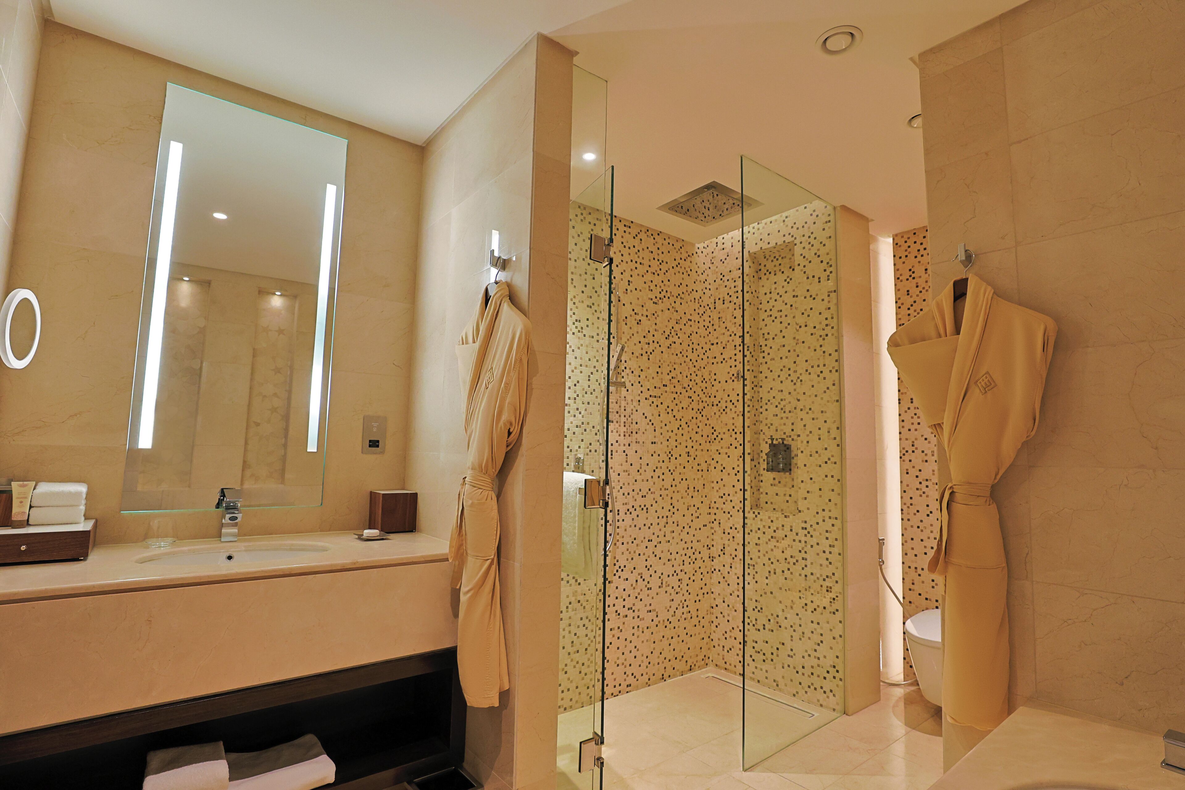 Un baño moderno con un espejo grande, una ducha con cerramiento de vidrio y dos batas colgadas en ganchos.