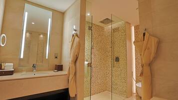 Un baño moderno con un espejo grande, una ducha con cerramiento de vidrio y dos batas colgadas en ganchos.