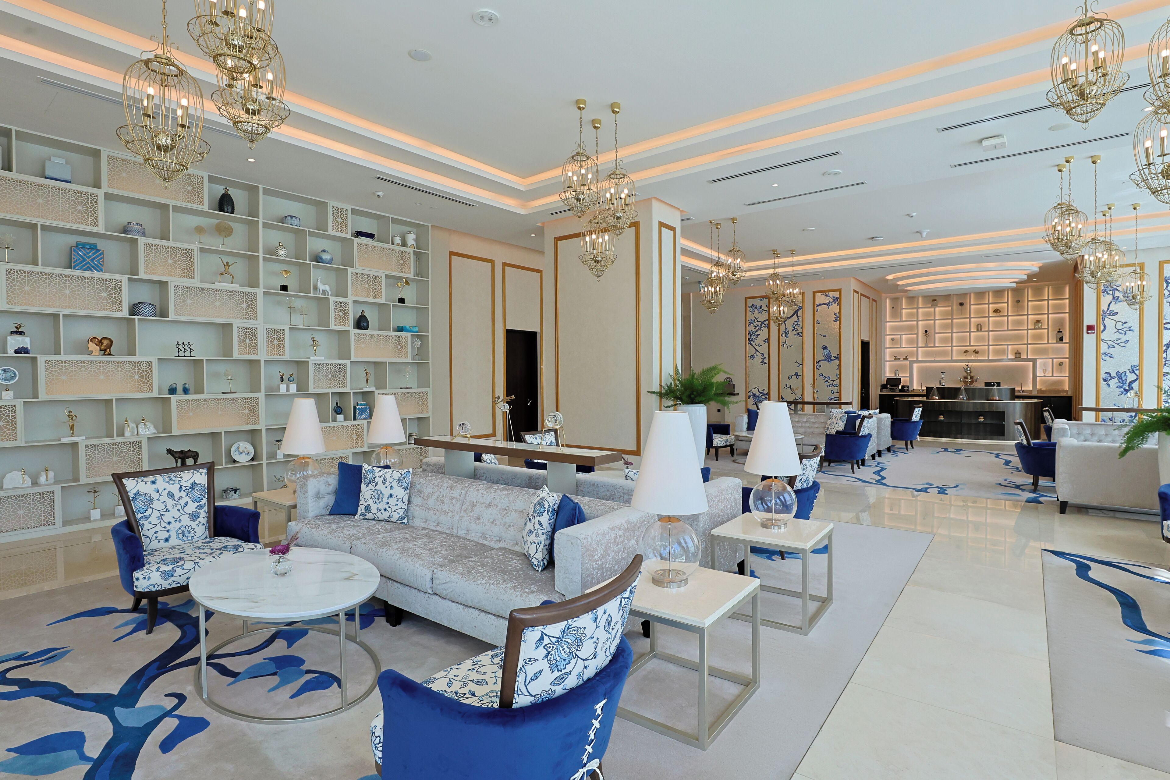 A spacious lobby with a sofa, chairs, and a coffee table, surrounded by shelves with decorative items and a bar area.