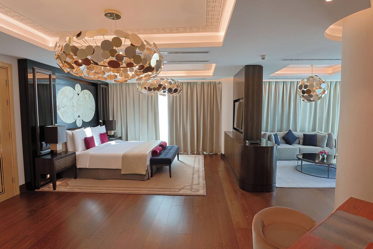 A modern hotel room with a large bed, a TV, a sofa, and a dining area.