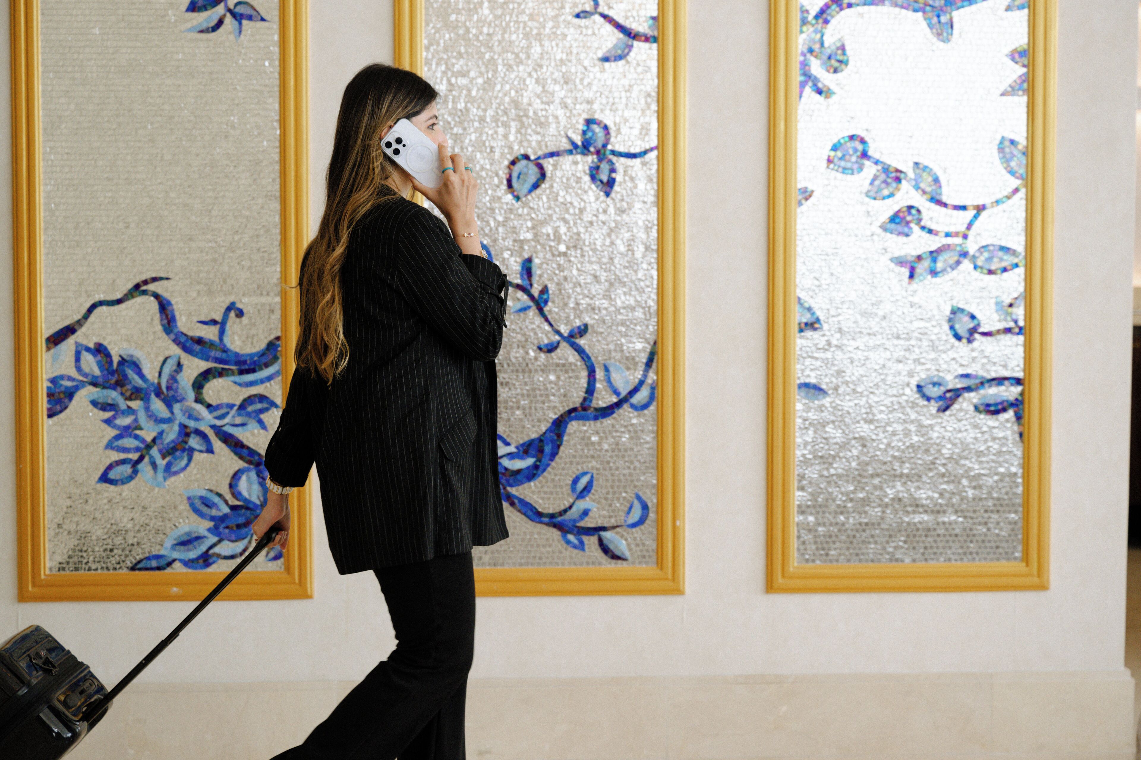 A person in a black pinstripe suit with a briefcase, standing in front of a wall with large, framed floral artwork.