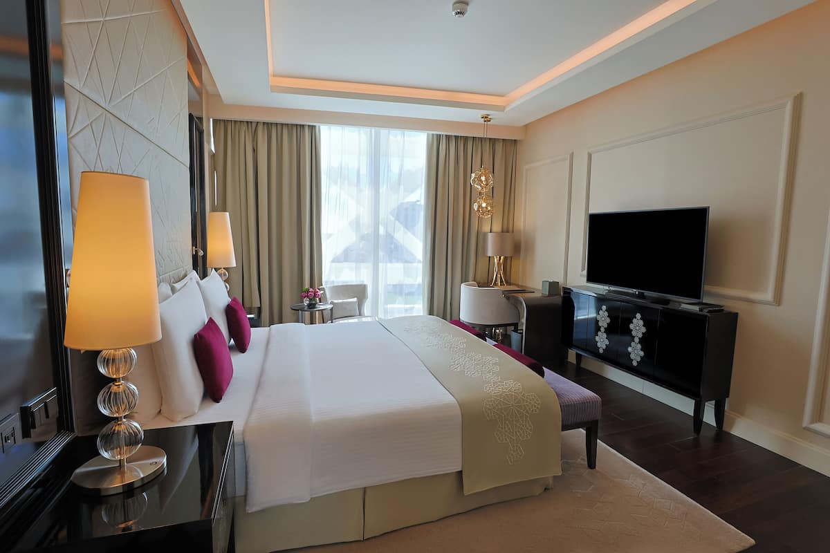 A hotel room with a large bed, a TV, a desk, and a view of the city.