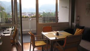 Ein Zimmer mit Tisch und Stühlen, einer Couch und Blick auf Berge durch große Fenster.