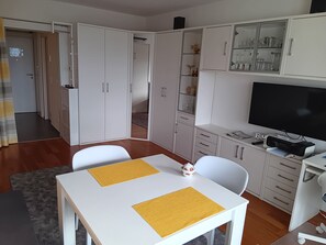 Ein modernes Wohnzimmer mit einem weißen Tisch, zwei Stühlen, einem Fernseher und einer Vitrine.