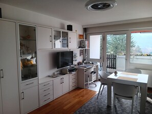 A modern kitchen with white cabinetry, a built-in TV, and a dining area with a table and chairs.