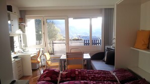 Ein Hotelzimmer mit zwei Betten, einem Schreibtisch, einem Stuhl, einem kleinen Tisch und Blick ins Freie.