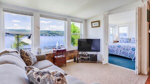 A cozy living room with a large TV, a sofa, and a view of a lake.