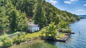 A two-story house with a deck overlooking a lake, surrounded by dense forest.