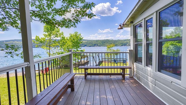 A wooden deck with a bench, a railing, and a view of a lake and hills.