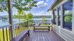 Una terraza de madera con un banco, barandilla y vistas a un lago y colinas.