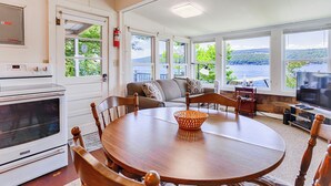 A cozy living room with a round wooden table, comfortable seating, a TV, and large windows offering a scenic view.