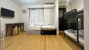 A compact room with a bunk bed, a desk with a chair, a flat-screen TV, a window with curtains, and an air conditioning unit. - Sadie's Home (Kawasaki)