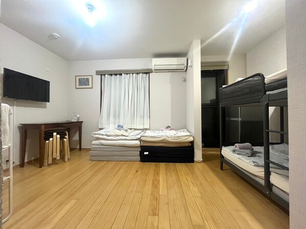 A compact room with a bunk bed, a desk with a chair, a flat-screen TV, a window with curtains, and an air conditioning unit.