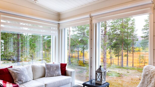 A cozy room with a white sofa, a black chair, and a view of a forest through large windows. - Villa taiga by Interhome (Raattama)