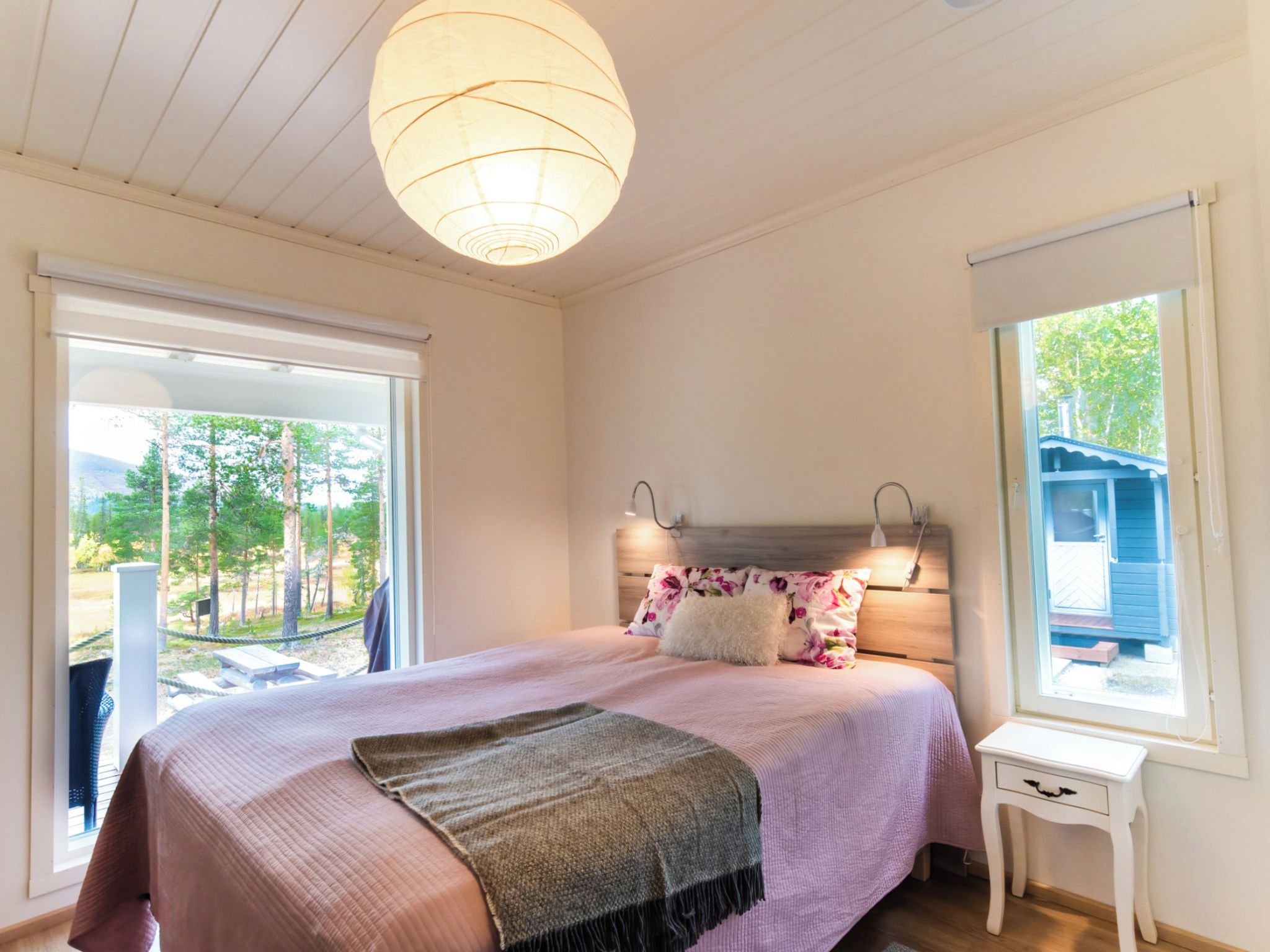 Un dormitorio con una cama, una mesita de noche, un colgante de luz y vistas al exterior.
