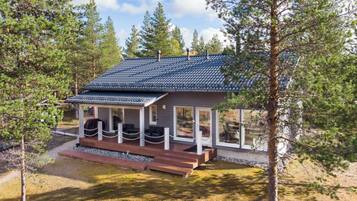 A cabin with a sloped roof, a porch with seating, and a view of the surrounding forest.