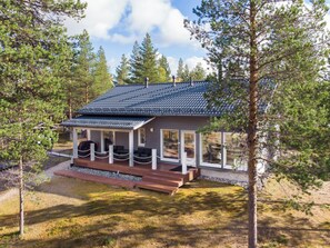A cabin with a sloped roof, a porch with seating, and a view of the surrounding forest. - Villa taiga by Interhome (Raattama)