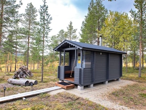 Eine kleine Holzhütte mit Veranda, Schornstein und Holzstapel in der Nähe.