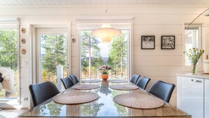 A modern dining area with a glass table, black chairs, and a view of trees through large windows. - Villa taiga by Interhome (Raattama)