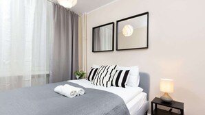 Una cama bien hecha con un edredón gris, una lámpara de noche y dos cuadros en la pared.