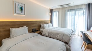 A hotel room with two beds, a desk, a chair, a nightstand, a lamp, and a painting on the wall. - Hotel The Grang Jungmun (Seogwipo)