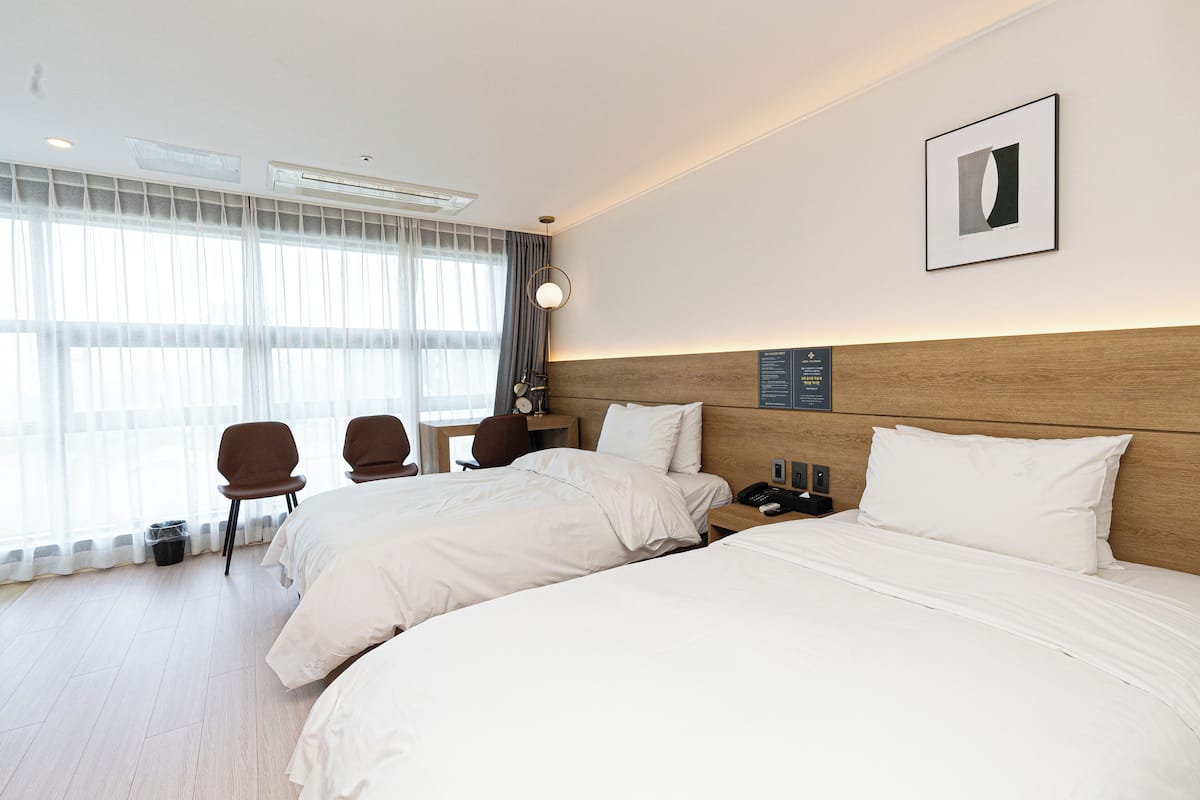 Ein Hotelzimmer mit zwei Betten, einem Schreibtisch, einem Stuhl und einem großen Fenster mit Vorhängen.