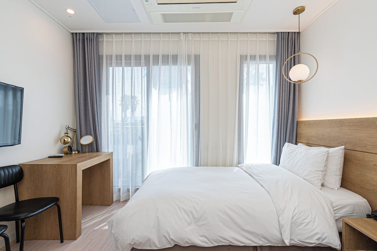 Ein Hotelzimmer mit Bett, Schreibtisch, Stuhl, Fernseher und einem fensterbepflanzten Fenster.