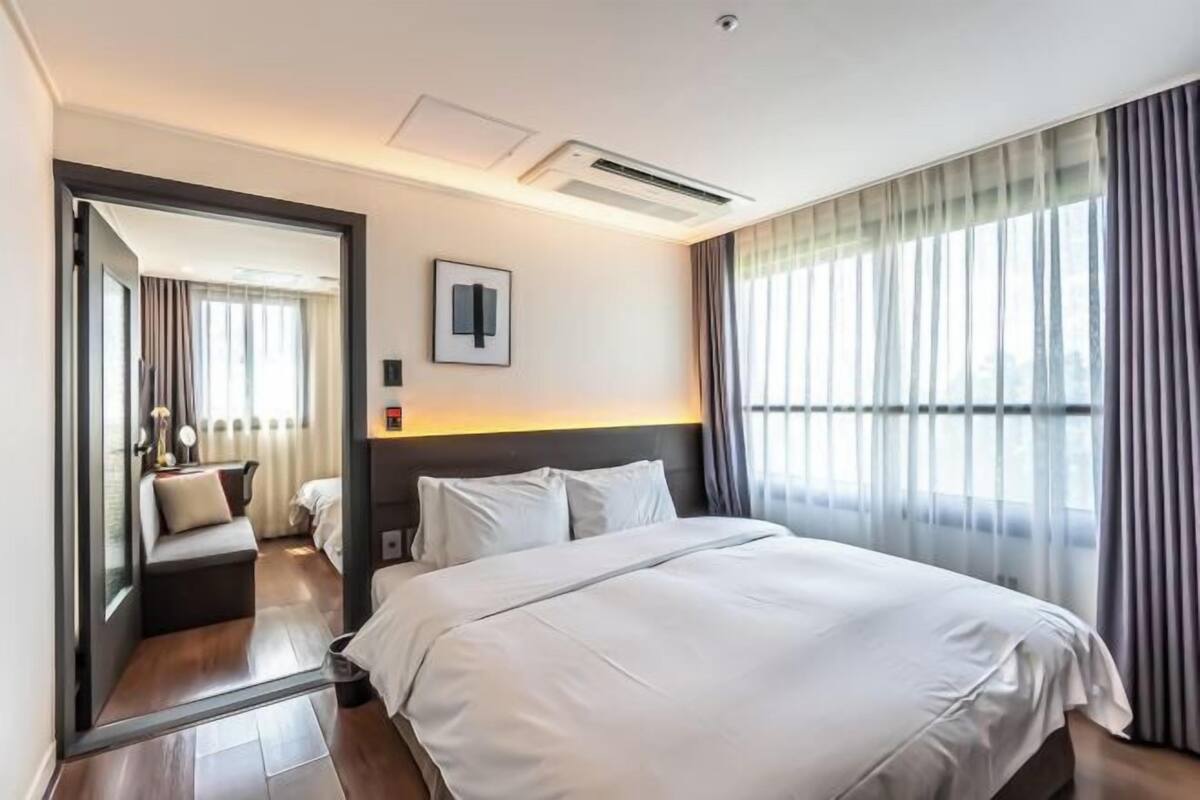 Ein Hotelzimmer mit einem großen Bett, einem Nachttisch, einem Spiegel und einem Vorhangfenster.