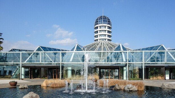 A modern building with a glass facade, a central water feature, and a distinctive tower structure. - Hotel The Grang Jungmun (Seogwipo)