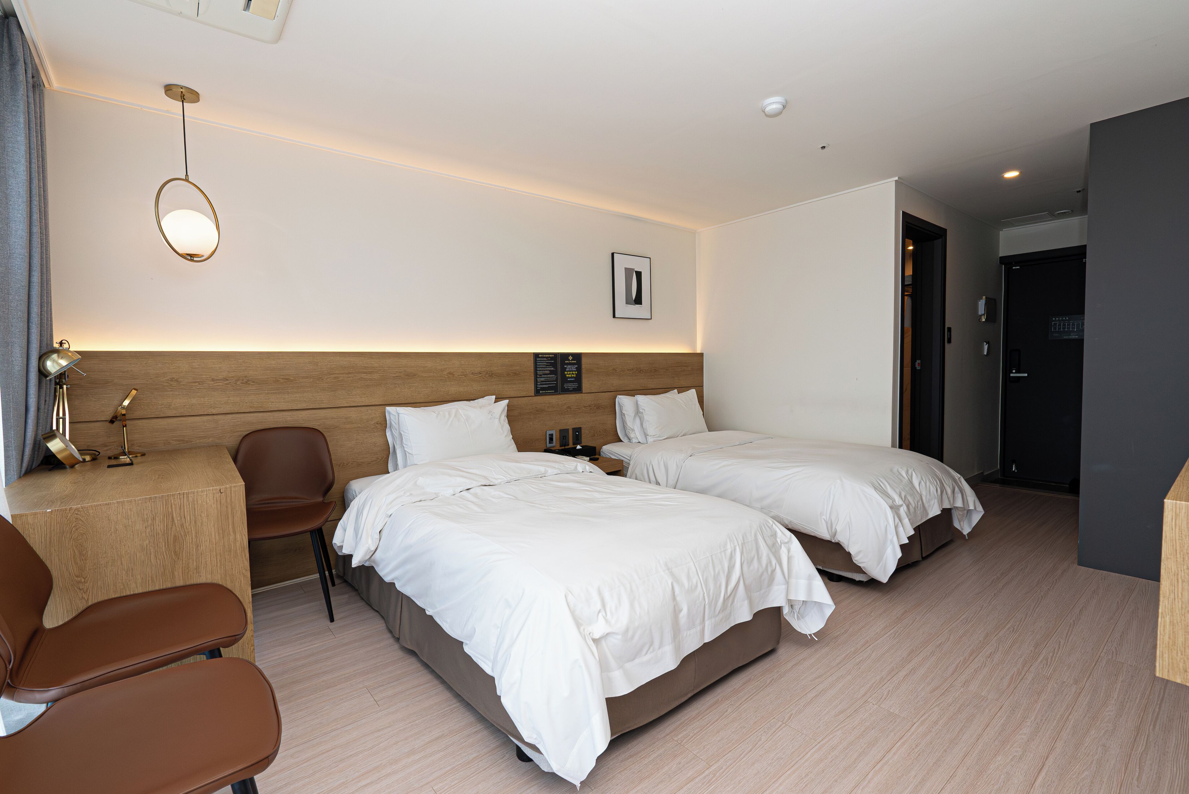 Une chambre d’hôtel avec deux lits, un bureau, une chaise et un luminaire fixé au mur.