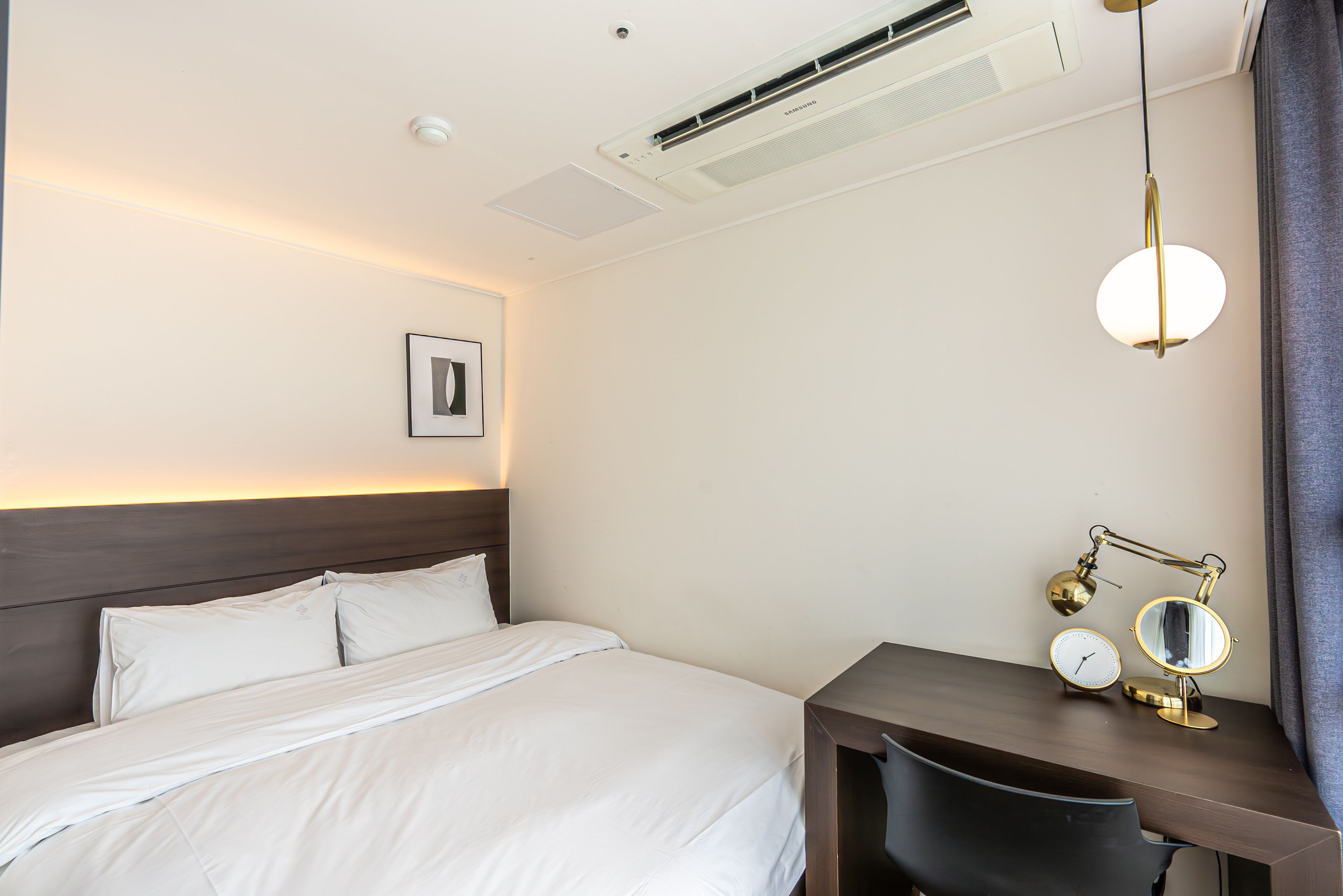 Une chambre d’hôtel équipée d’un lit, d’un bureau avec une lampe, d’une horloge et d’un appareil de climatisation.