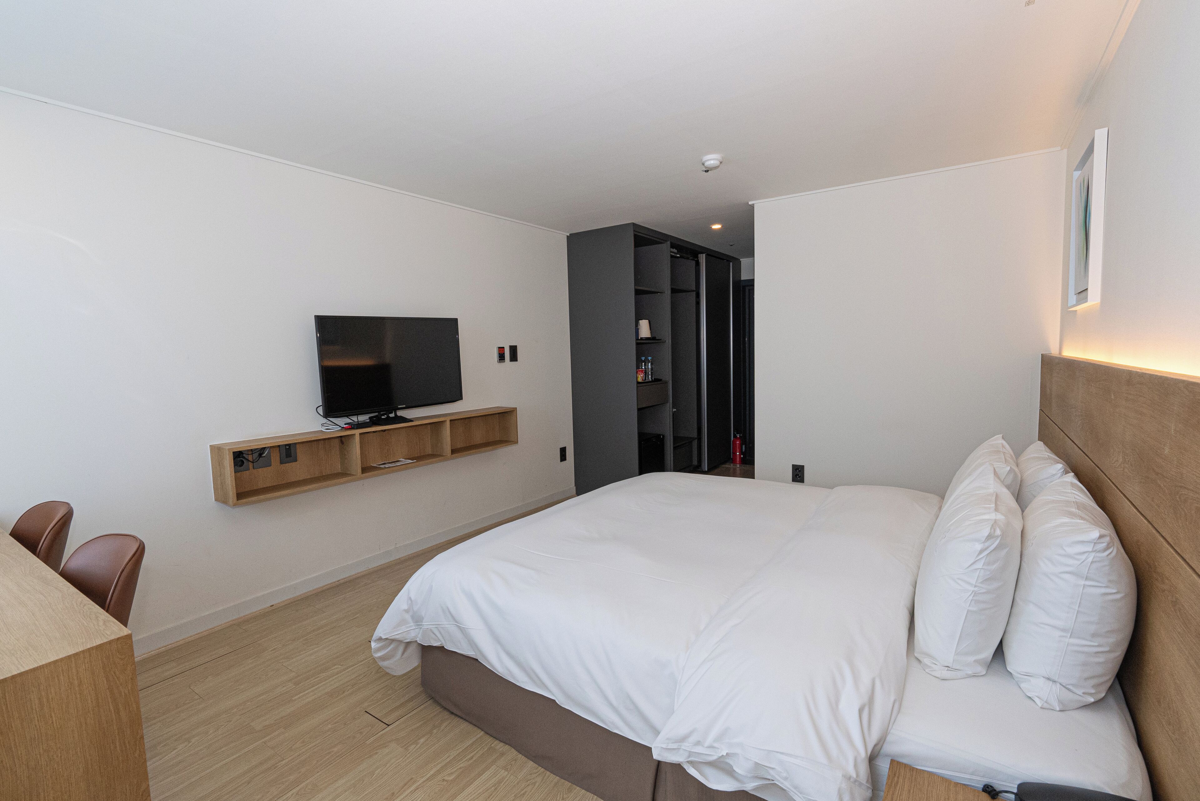 Une chambre d’hôtel moderne avec un grand lit, un téléviseur fixé au mur, un bureau en bois et une armoire.