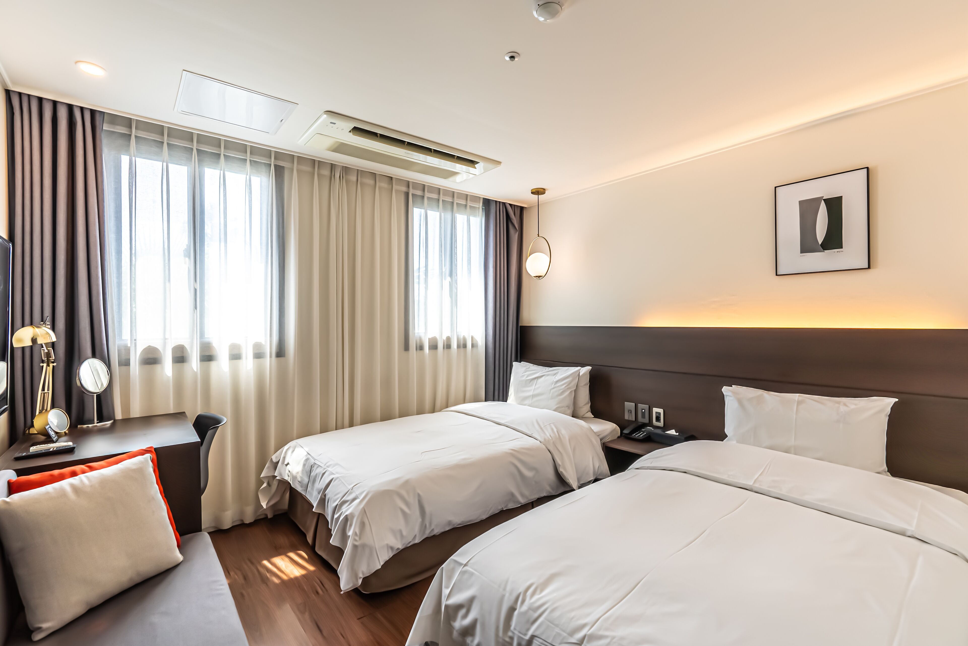 Une chambre d’hôtel avec deux lits, un bureau, une chaise, une lampe et une table de chevet avec un téléphone.