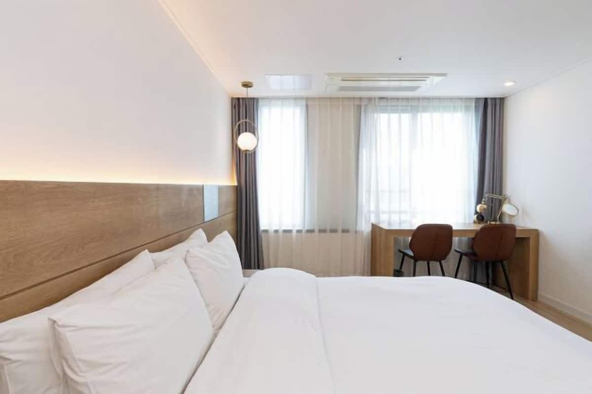 Ein Hotelzimmer mit einem großen Bett, einem Schreibtisch mit zwei Stühlen und einem fenster mit Vorhängen.