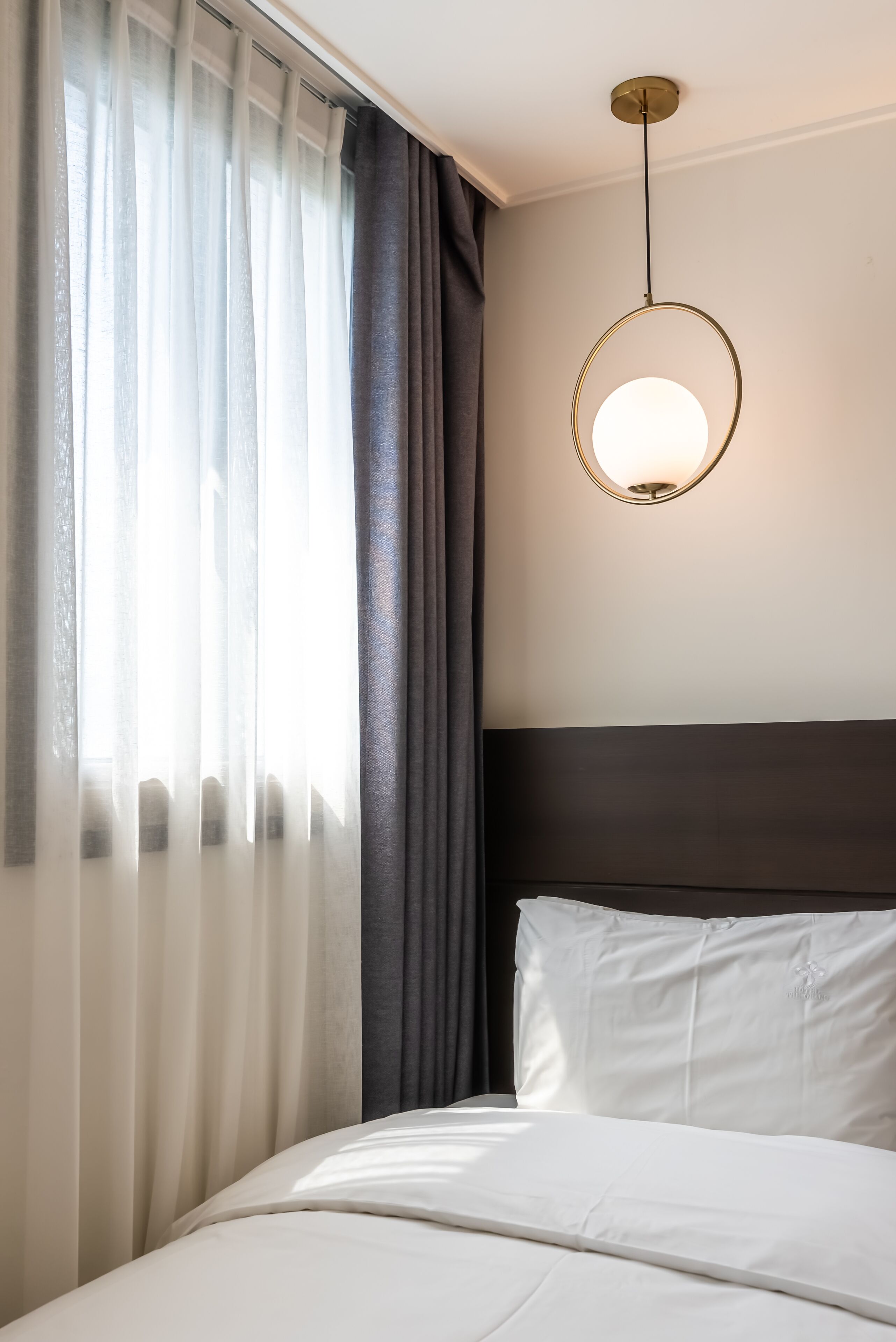 A hotel room with a bed, curtains, a headboard, and a hanging light fixture.