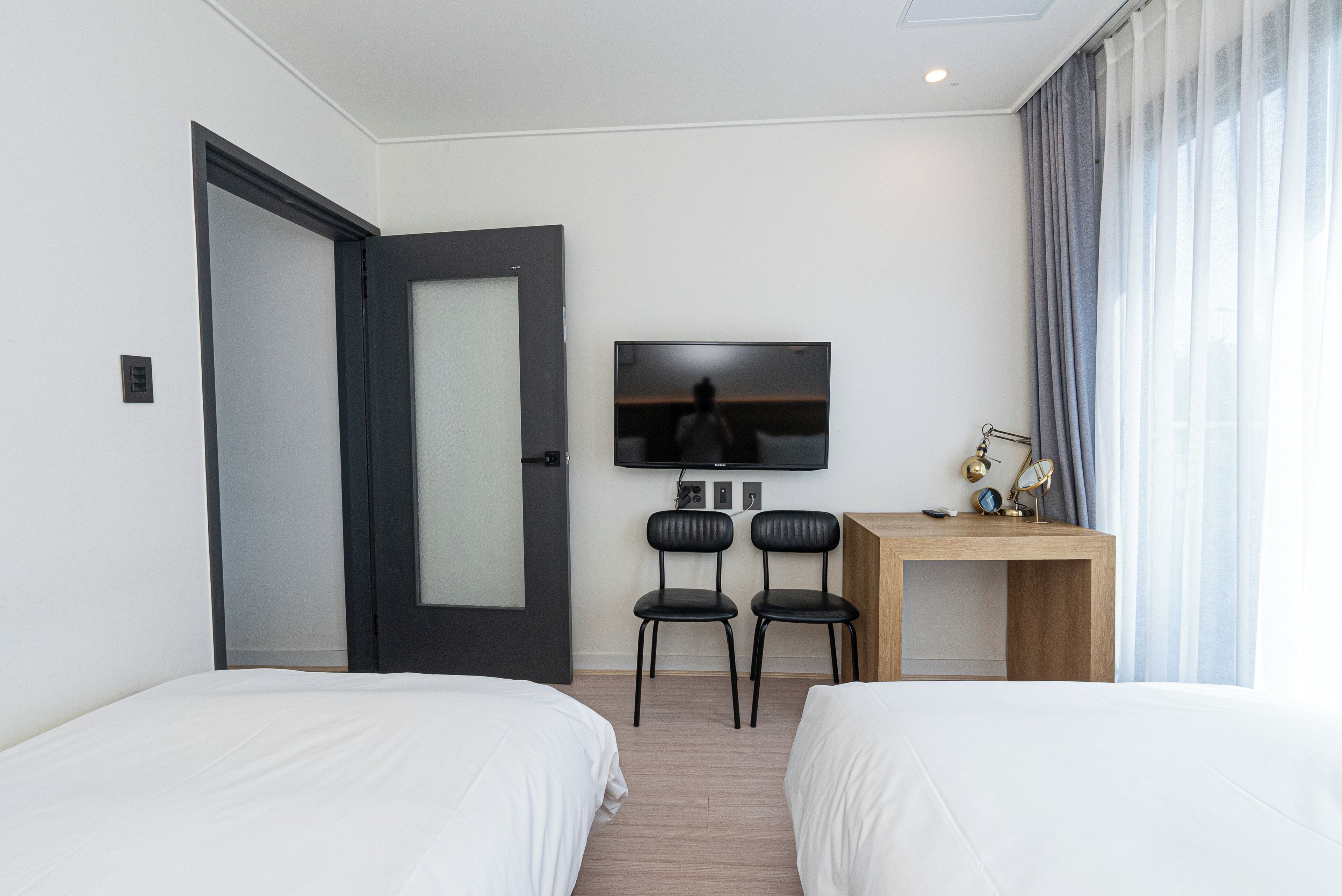 A hotel room with two beds, a desk, a TV, and a door.