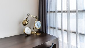A modern hotel room with a dark wooden desk, a round table lamp, a wall-mounted clock, and sheer curtains allowing natural light. - Hotel The Grang Jungmun (Seogwipo)