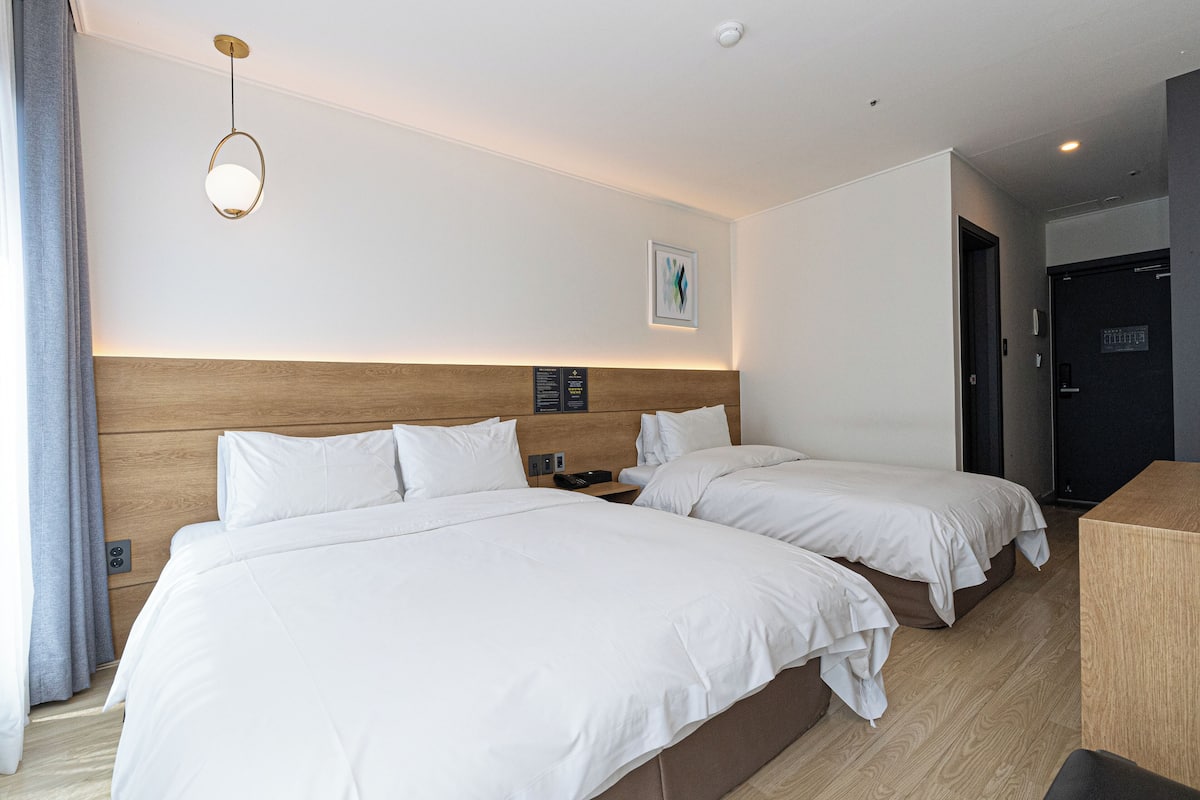 Ein Hotelzimmer mit zwei Betten, einem hölzernen Kopfteil, einem Nachttisch mit Telefon und einer Wandleuchte.