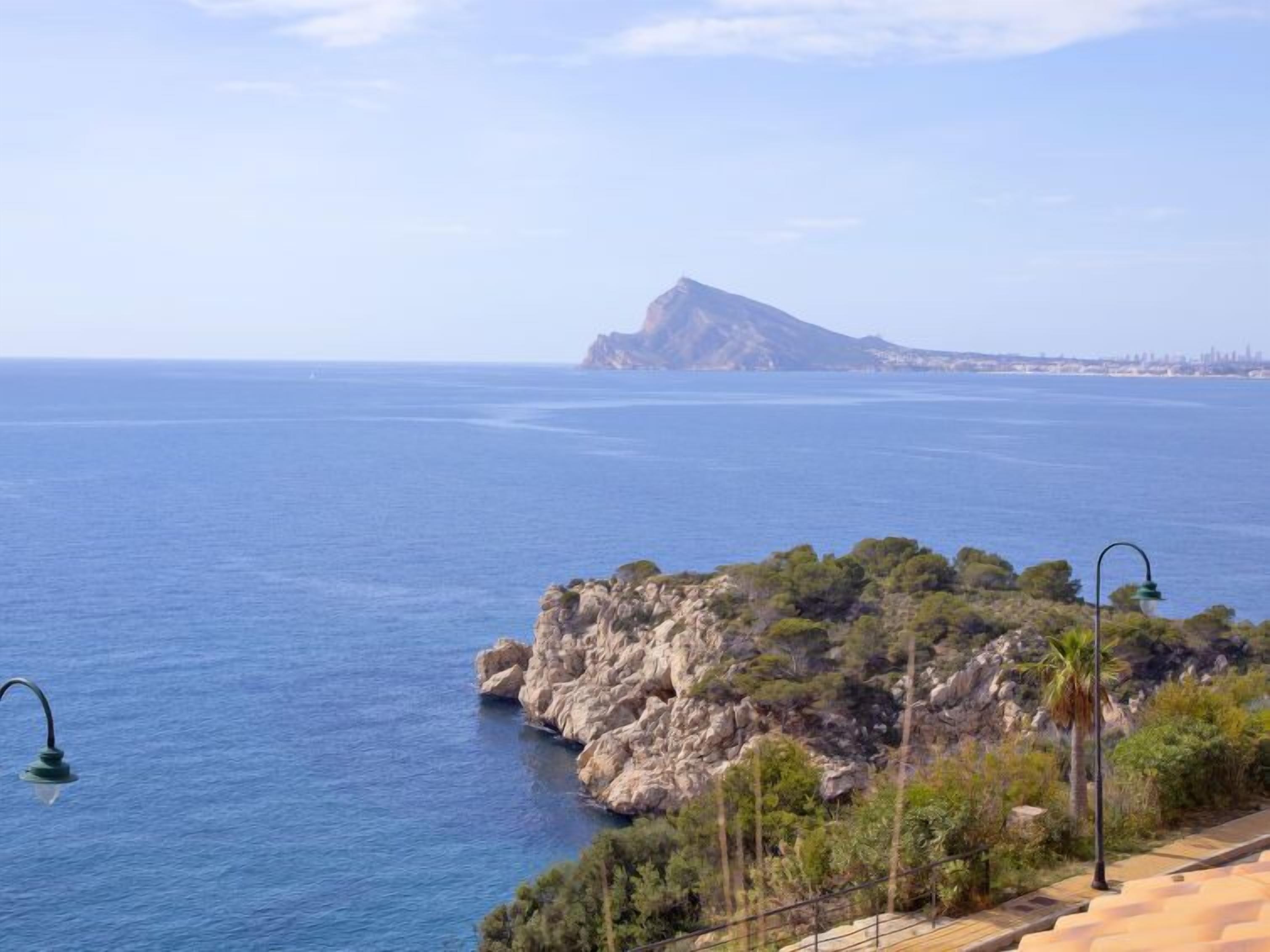 A coastal view with a rocky outcrop and a distant mountain.