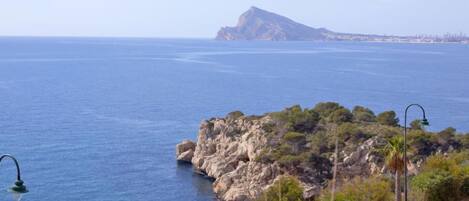 A coastal view with a rocky outcrop and a distant mountain.
