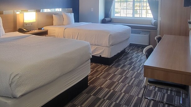 A hotel room with two beds, a desk, a chair, a TV, and a window with curtains. - Microtel Inn & Suites by Wyndham Fountain/Fort Carson (Fountain)